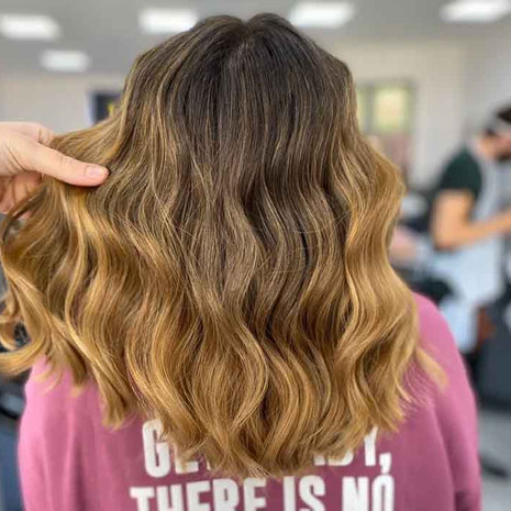 Client is facing back showing her new hair colour, which is a caramel half-head balayage, wavy medium long hair