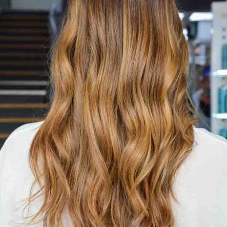 Client is facing back showing her new hair colour, which is a half-head balayage in golden blonde tones, long wavy hair