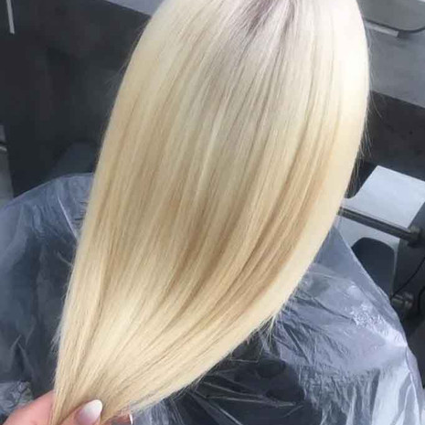 Client is sitting at the hair stylist station facing to the back, showing her new hair colour which is a global root bleach, bleach blonde hair