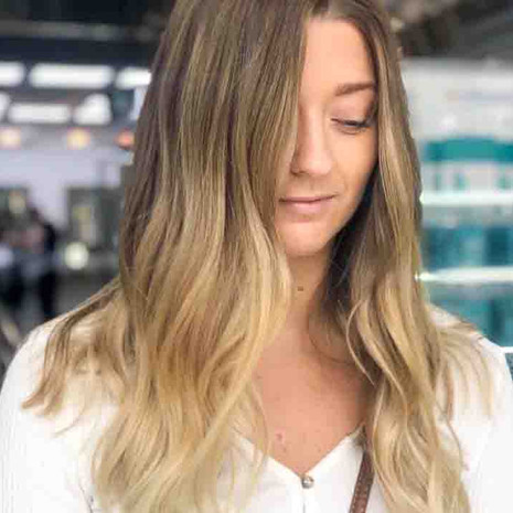 Client is facing front, looking down showing her new hair colour, which is a vanilla and honey tone half-head balayage