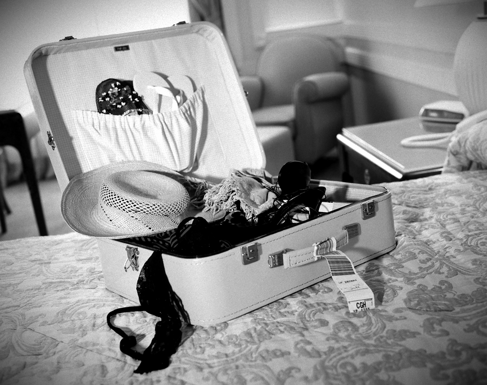 Black and white image of an open suitcase on a hotel bed