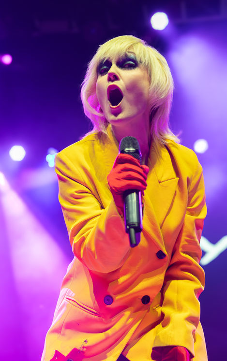 Person singing passionately on stage with vibrant lighting.
