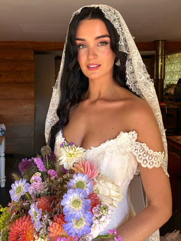 Bride in a lace wedding dress holding a pink and white bouquet with radiant bridal makeup