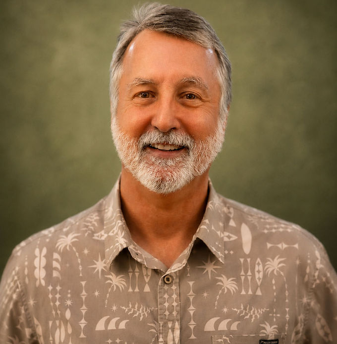 Smiling man with gray short hair and a white beard wearing a brown and tan print button up shirt.