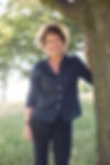 Jeanette Winterson smiling, backlight creating a halo around her head, hand against a tree