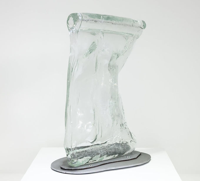 Ghost Optics
April 2 through December 31, 2026
Visitors to the Museum of American Glass will encounter a site-specific window intervention by guest artist and curator, Jocelyne Prince. Her work, Ghost Optics, addresses early methods of flat glass and bottle glass production. Of particular interest to the artist was the variety of Americana imagery found on the historic glass bottles in the collection. Wanting to source these images as directly as possible, Prince dug into the WheatonArts mold collection and honed in on one particular mold, a flask for spirits, which had an inset for interchangeable emblems. The imagery for these emblems was a mix of patriotic, historic, and commemorative motifs. This mold was part of an industrial technology known as the “American System.” Similar to industrial advances in other kinds of production, the glass industry capitalized on a bottle mold with interchangeable parts – in this case an assortment of emblem inserts meant that one mold could be used to make a multitude of different bottles.
Working with the Paul Wissmach Glass Company in West Virginia, Prince hot cast the various emblems and then fed them into the industrial glass roller. The emblems are stretched, crackled, and sometimes even fractured—their ghost-like watermark characteristic becomes visible at certain angles and invisible at other angles. This material process mirrors how we test our patriotism and democracy. . . challenging its limits, and sometimes going beyond.
Portals and Passages
April 2 through December 31, 2026
Curator Jocelyne Prince has brought together five artists: Justin Ginsberg, Romina Gonzales, Ashley Raye Harris, Matthew Day Perez, and Alexander Wenstrup, who have an acute understanding of how just a few millimeters of glass can shift our perception of the world. Each work in this exhibition catalyzes the optical and sculptural space that exists within a sheet of glass. In some cases, the surface of the glass has been disrupted, or bears the marks of the action of its making, or the glass composition has been specially concocted to refract light, or the tiniest amount of air is trapped and visually manifested. A fascination with surface, the space just beyond the surface, what we see through the glass, the space within the glass, and what we see reflected in the glass preoccupies these artists.
The works in this exhibition have been selected in conjunction with, and as a complement to the research and activities that are part of the November 2026 WheatonArts symposium on window glass production methods, “Transparent Thresholds.”