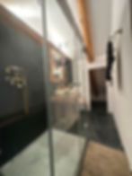 Badezimmer im Solforo mit begehbarer Glasdusche, dunklem Steinboden und sichtbaren Holzbalken.