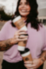 Smiling tattooed woman holding three stacked coffee cups