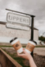 Two Uppers coffee cups held in front of the shop sign
