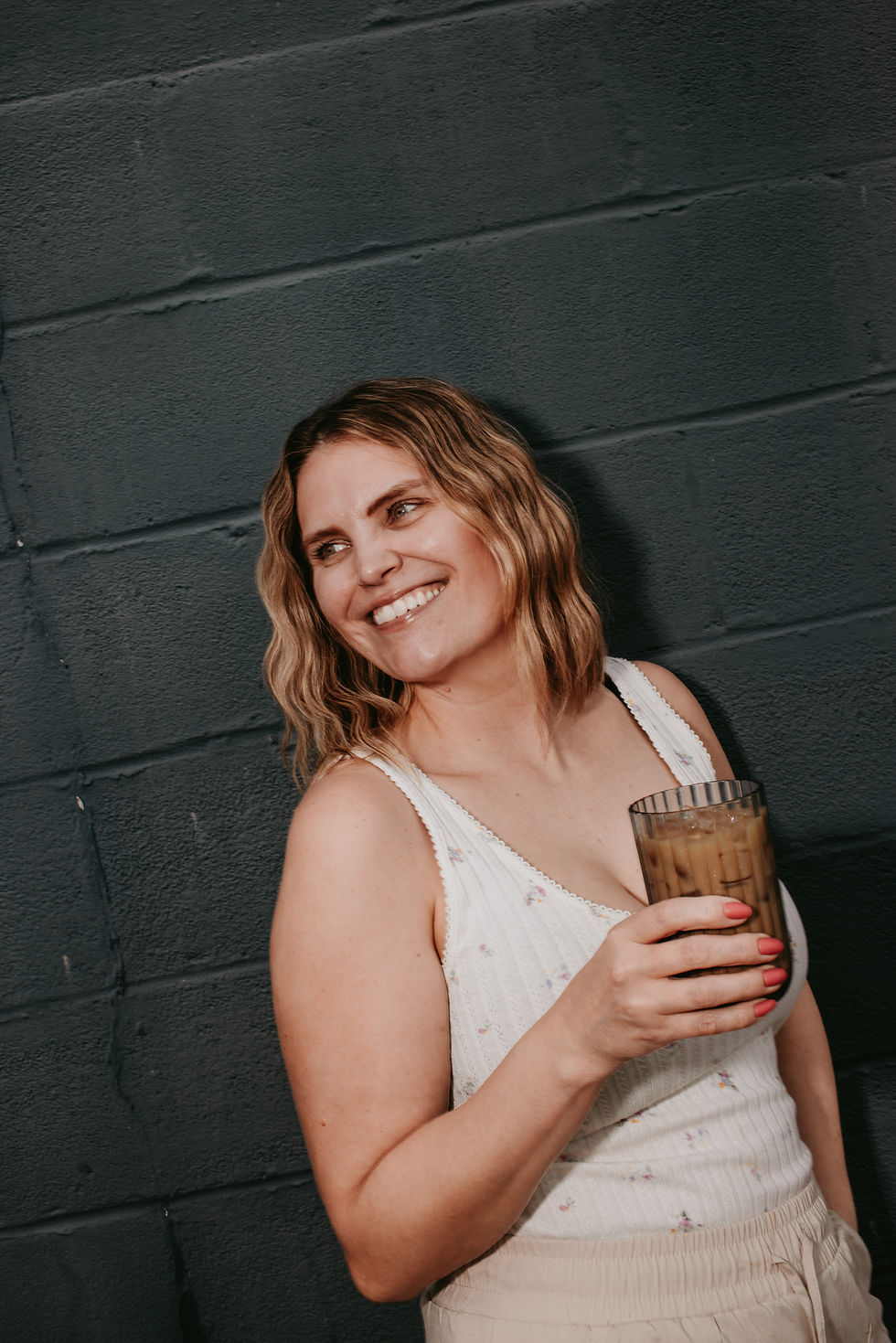 Smiling woman holding an iced coffee against a dark wall