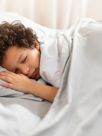 A young African American boy is peacefully sleeping in a bed with crisp white sheets cover