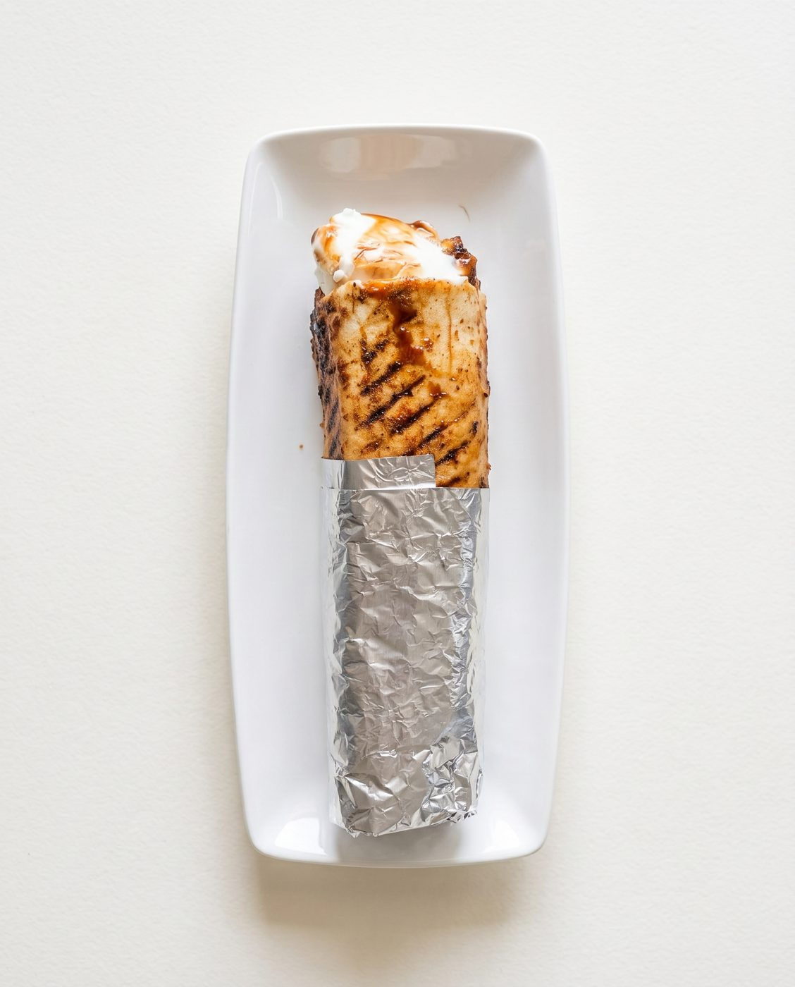 Best viral crispy shawarma wrap in Windsor Ontario — overhead grill-pressed chicken shawarma wrap half in foil on a white plate at Aromas Cafe by 7Spices