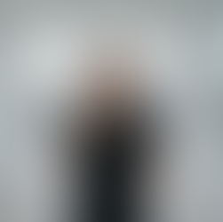 Smiling clinical research coordinator in black scrubs stands in a modern office with New York City skyline visible through large windows. Bright, professional setting.