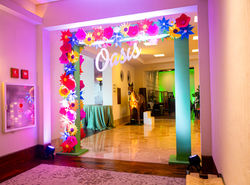 Arco de entrada personalizado con flores gigantes coloridas y letrero iluminado "Oasis", diseñado po