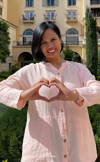 A smiling woman showing a heart hand sign.