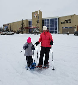 An adult and a child using snowshoes in the snow, walking together through a wintery landscape, enjoying the outdoors and the