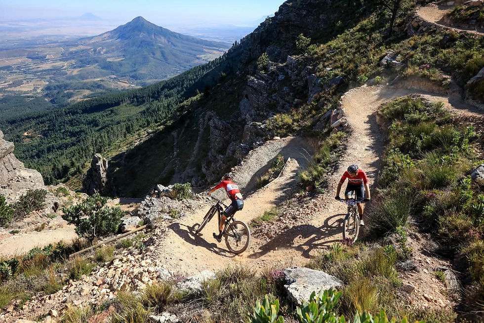 Two riders on mountain bike trails with panoramic mountain views.