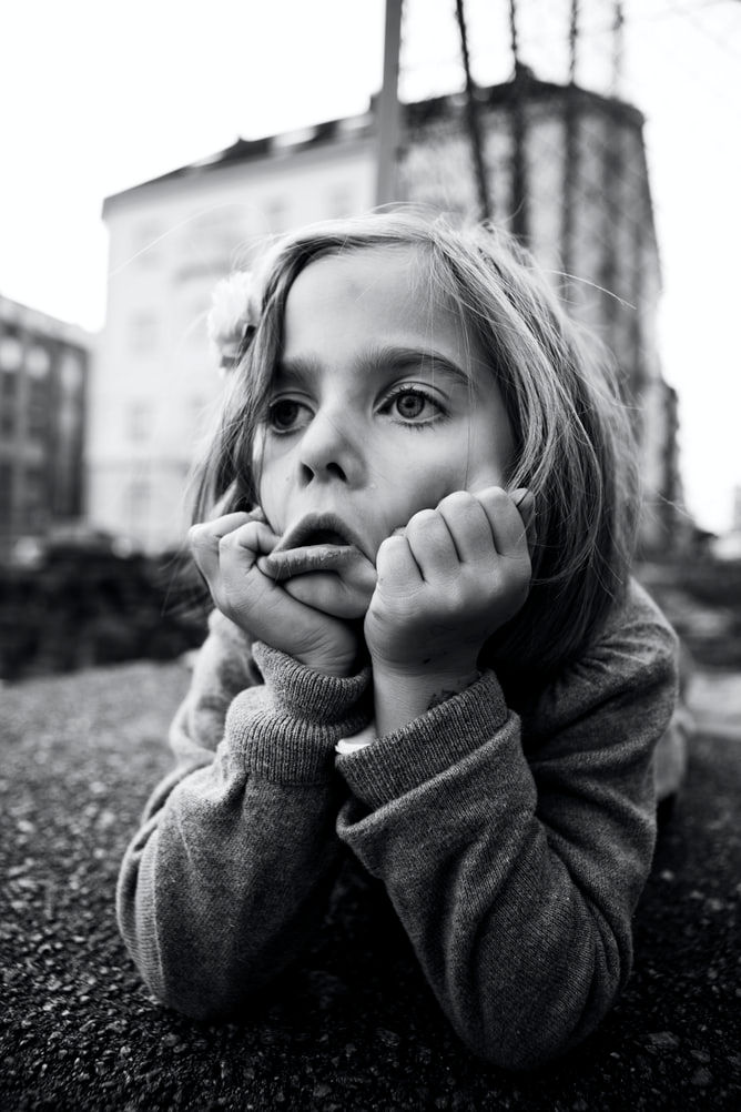 Girl sitting outside with her hands under her chin, on the ground.