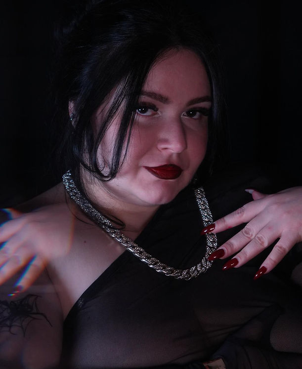 Mistress Kaizen in s dreamy photo showing her dominant personality looking directly to the camera. the domme has a seductive glance over the submissive with shap long burgundy stiletto nails to scratch slave in her dungeon in the city center