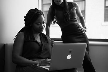 A woman on a laptop and another woman standing over her and looking at the laptop screen