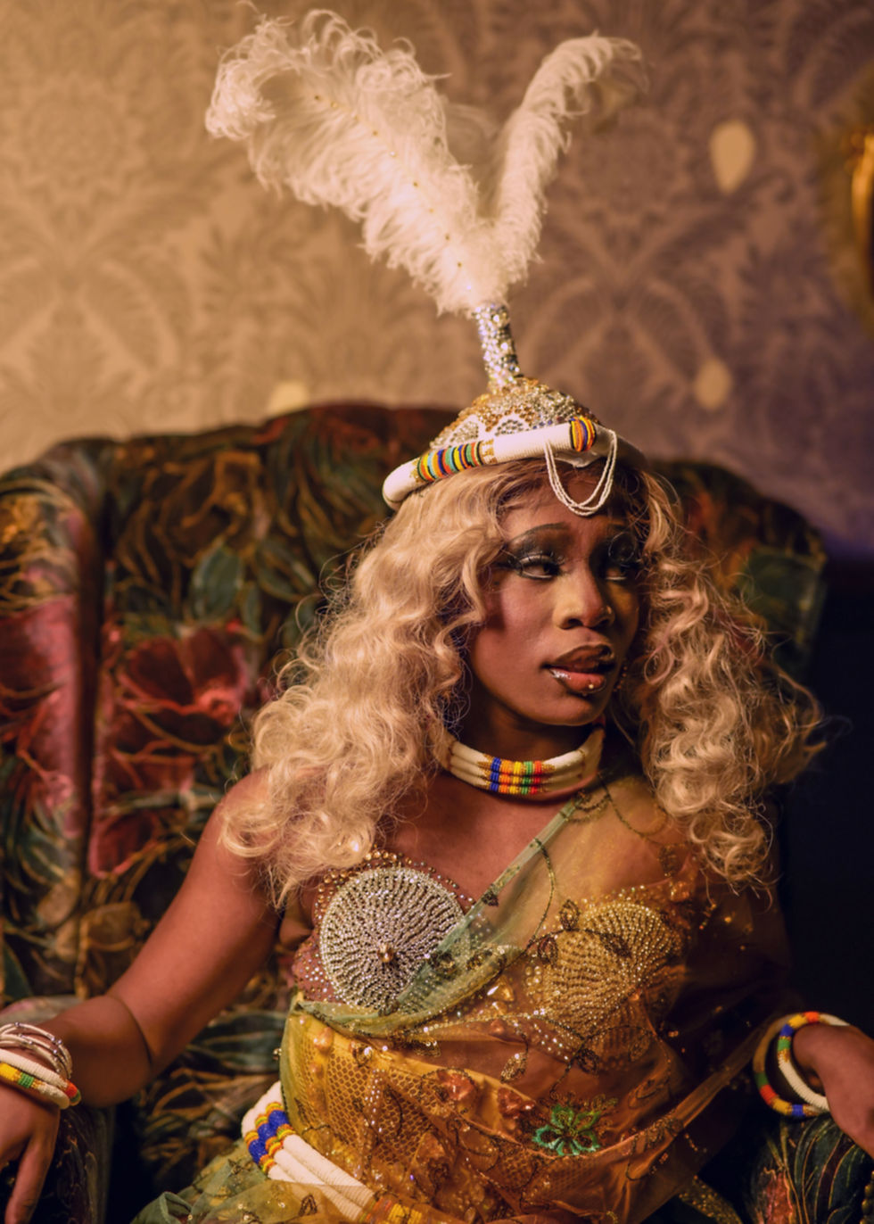 Drag queen sitting in chair with Zulu accessories.
