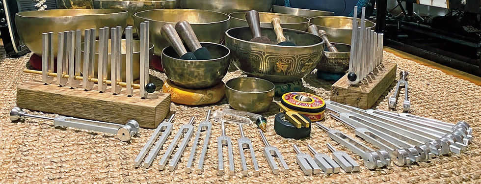 Tuning forks and Tibetan singing bowls on a woven mat. Mallets are inside the bowls, creating a calm and serene atmosphere.