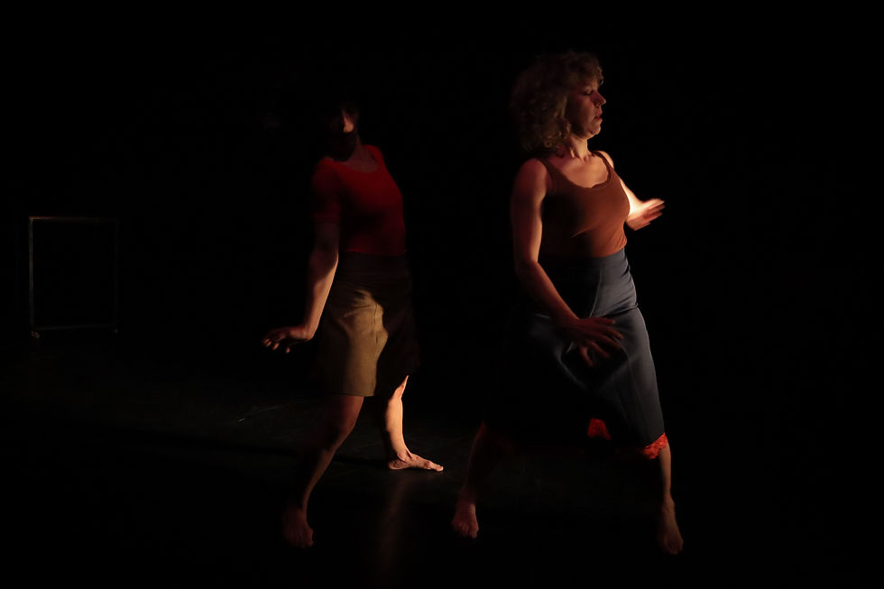 Dos bailarinas en un escenario oscuro, iluminadas en rojo, con movimientos suaves y expresión concentrada. Atisbos de un ocaso