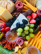 A gourmet charcuterie board with artisan cheeses, blackberries, green grapes, honey, cured meats, bread, and chocolates, arranged for an elegant presentation.