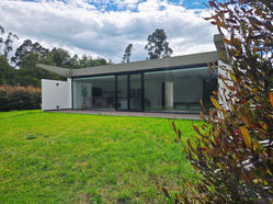 Modern house with glass walls, green grass, and a cloudy sky. CasaGuasca