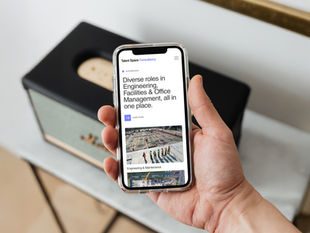 A hand holding an iPhone displaying the Talent Space Consultancy website, showcasing diverse roles in engineering, facilities, and office management on the homepage.