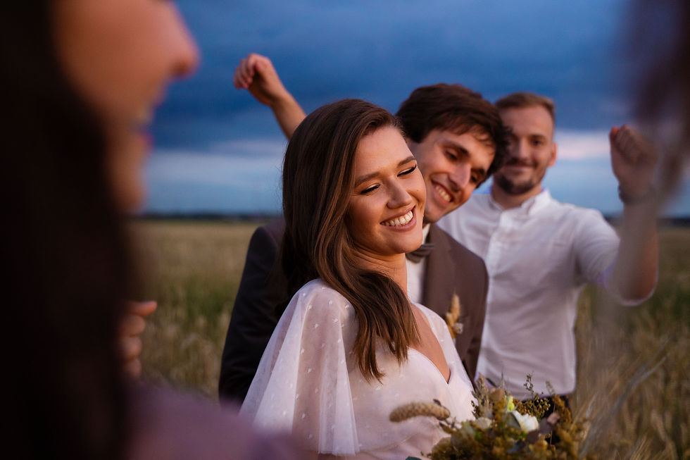 Smiling bride and groomsmen at an outdoor wedding in a grassy field under a cloudy blue sky.
