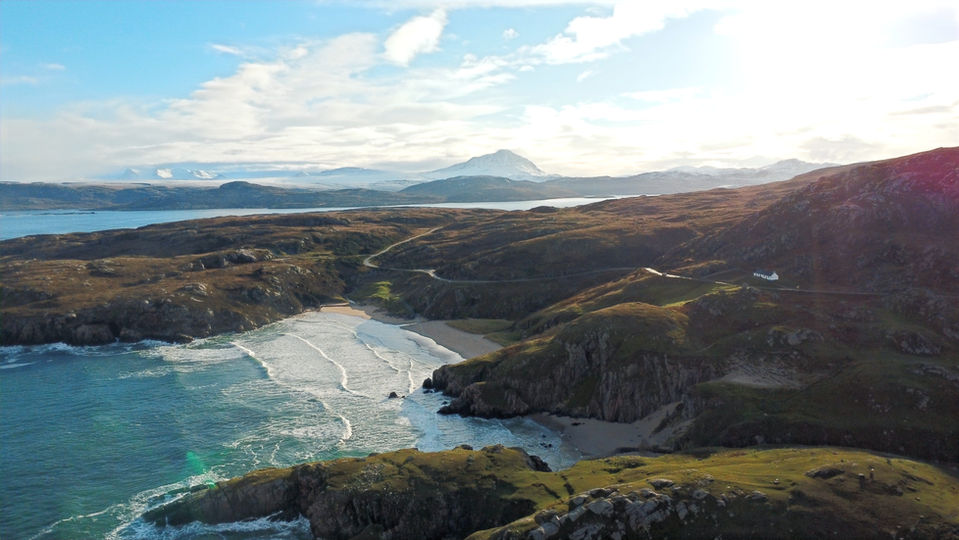 Ceannabeinne Cottage aerial view above Ceannabeinne Beach, Scottish Highlands holiday let with ocean and Ben Hope and Ben Loyal in the background.