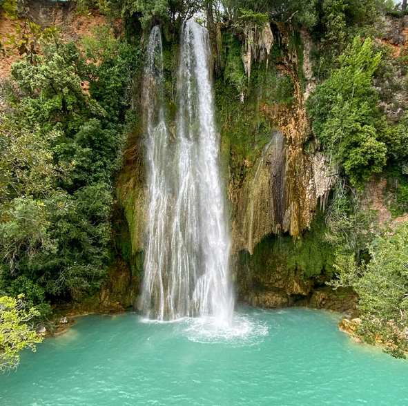 Waterfall in Provence cascading into the turquoise water, surrounded by lush green vegetation.