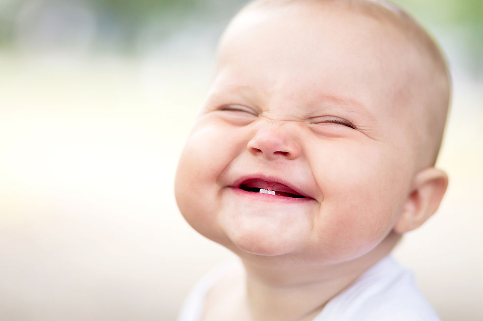 Smiling baby with closed eyes shows first tow bottom teeth.