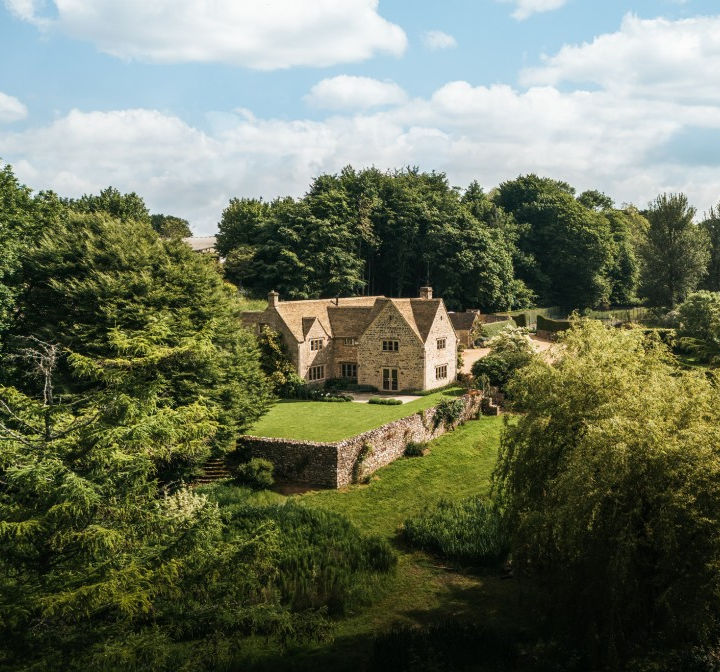 Large stone house in the English countryside surrounded by trees on a sunny day