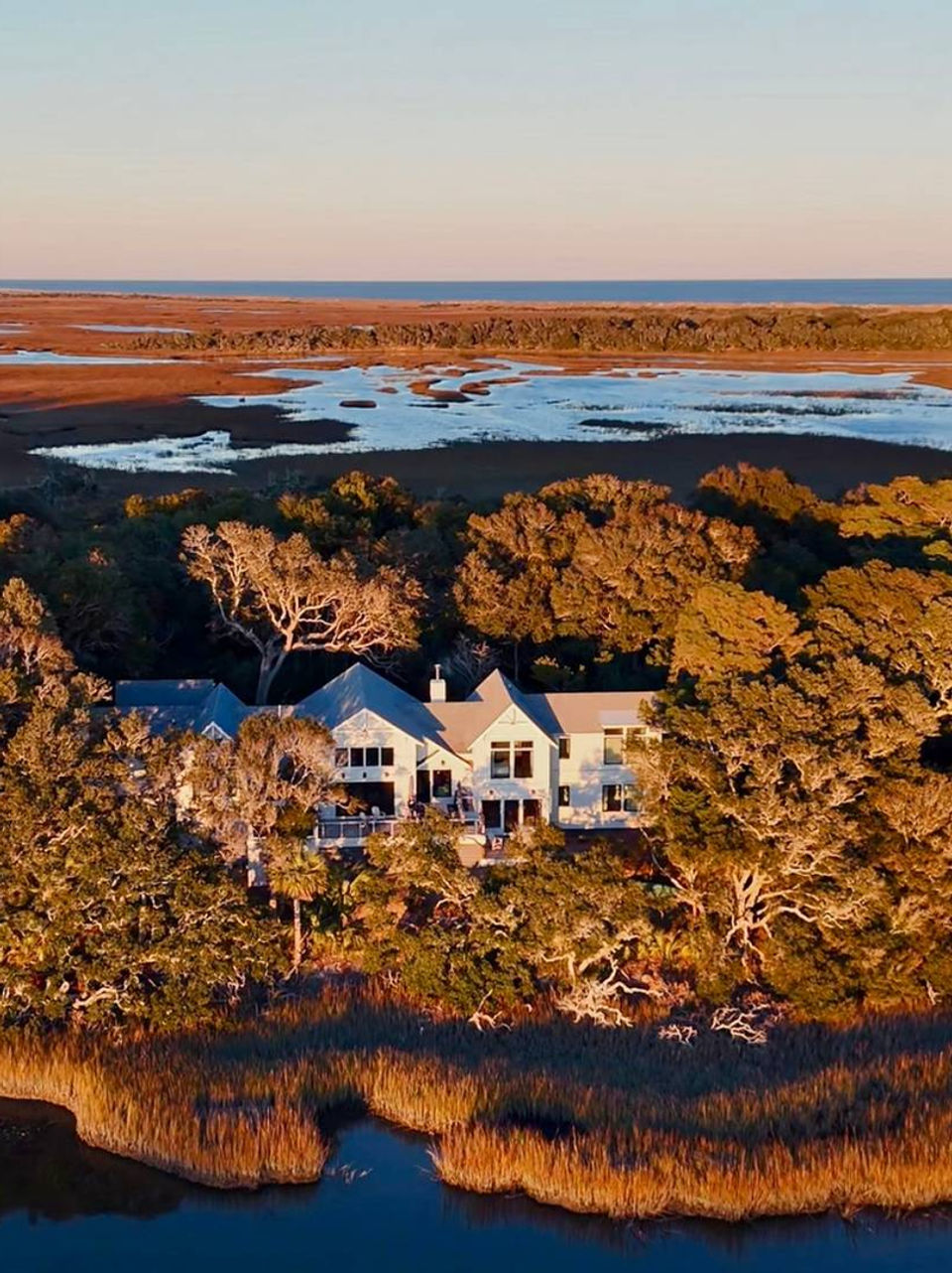 Large house at sunset overlooking water surrounded by trees, landscape view.