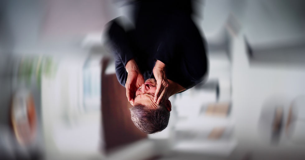 Middle-aged man squinting his face and holding his temples. Background is blurry.