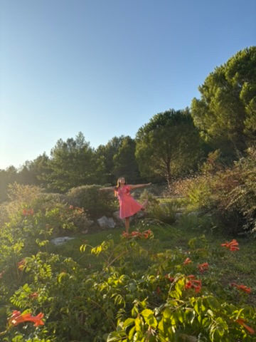Face to the brilliant blue sky, arms open wide, surrounded by trees and wild flowers