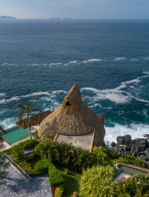 Luxury coastal villa in Zihuatanejo with thatched roof overlooking the ocean; tropical paradise.