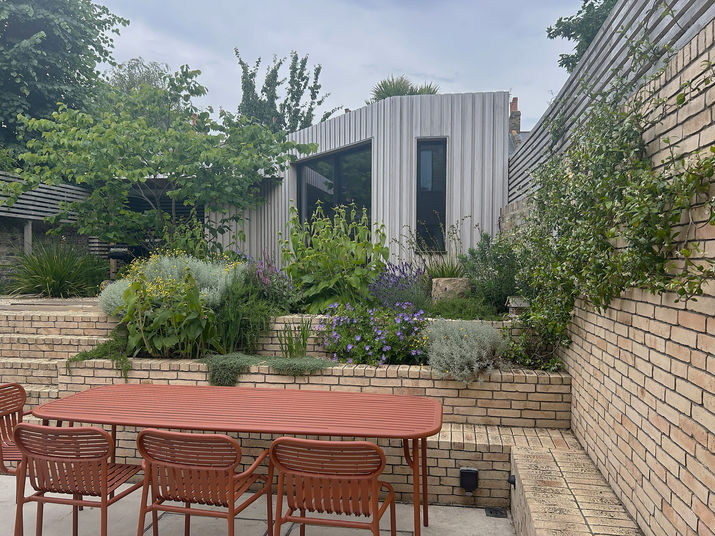 A red outdoor dining table and chairs set on a stone patio below tiered garden walls.