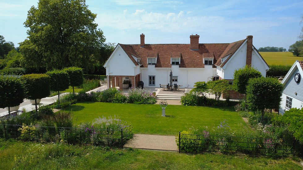 Country estate garde n designed to enhance the grade II listed property with formally arranged borders containing naturalistic planting and topiary trees, surrounding a central lawn.