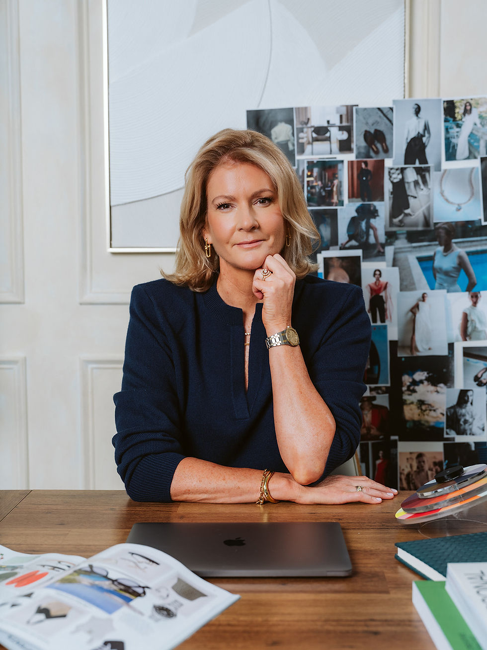 Personal stylist Suzanne sitting at her desk with a mood board and laptop, leaning her chin on her hand in a navy sweater.