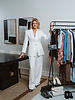 Personal stylist standing in a bright, modern studio beside a curated clothing rack featuring women's fashion, handbags, and shoes.