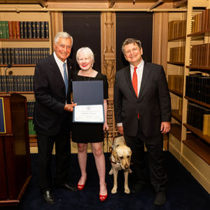 Marissa holding a certificate and posing with two men who are part of the Landegger family in a library.