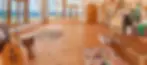 Sunlit room with wooden floors, patchwork cushions, a drum, lute, and clarinet. Ocean view through large windows. Cozy, artistic vibe.