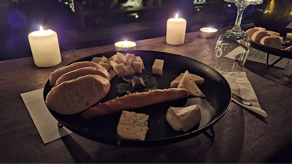 Cheese and bread on a dark plate, surrounded by lit candles on a rustic wooden table. A wine glass stands nearby, creating a cozy ambiance.