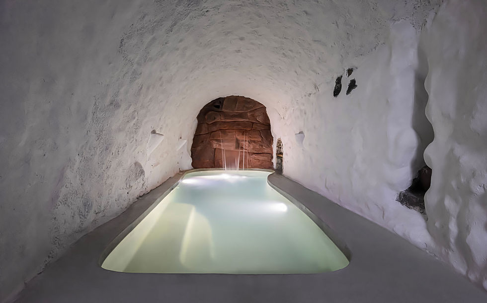A serene pool with gentle lights is set in a white, cave-like room. The arched ceiling and textured walls create a tranquil, spa-like ambiance.