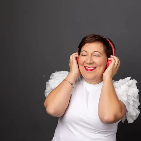Smiling woman in red headphones and a white ruffled top, eyes closed against a dark gray background.
