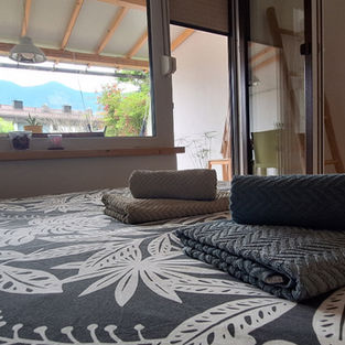 Cosy and inviting Green Garden Studio with fresh towels neatly arranged on a patterned bedspread, offering a serene view of the terrace and distant mountains through large windows.
