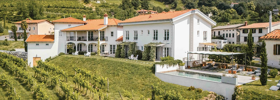 Large white villa with red roof, surrounded by lush vineyards and greenery. Outdoor pool, patio seating, and scenic hillside setting.